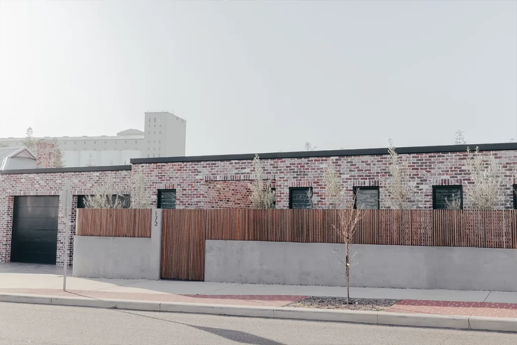 Rough brick, one-level home with render and wood mixed fence in front. Two single garages on the left.